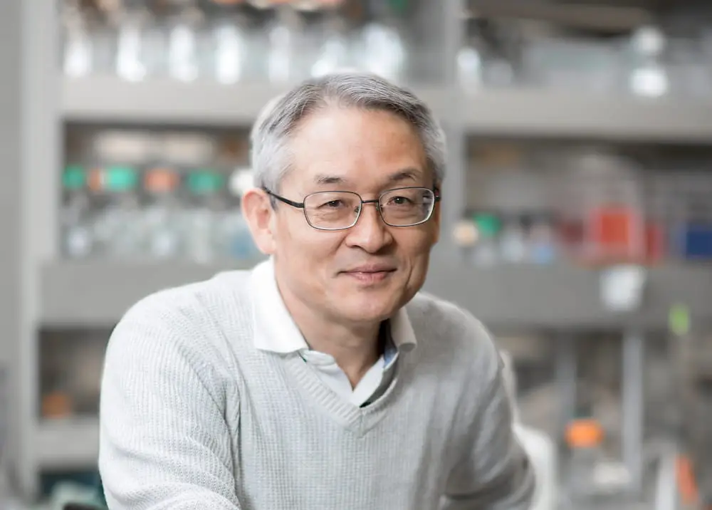 Photo portrait of Professor Toshiaki Kawakami, M.D., Ph.D. He is sitting in a lab setting and smiling