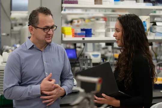 Photo of Ay (left) Salgado-Figueroa talking in a lab setting