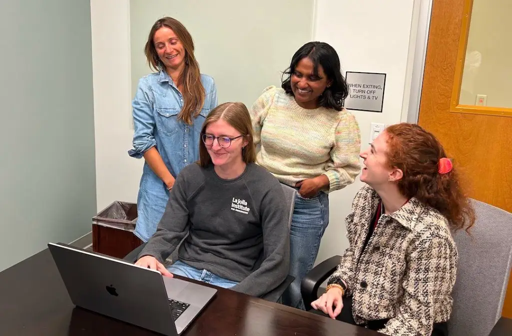 Four LJI scientists surrounding a laptop computer in a lab setting