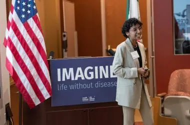 Photo of LJI scientist speaking to a group in the seminar room. There are American and Mexican flags in the background