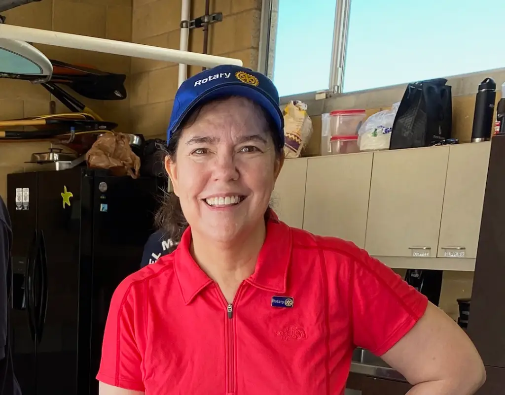 Sharon Schendel looks at camera and smiles. She is wearing a blue cap and red polo shirt