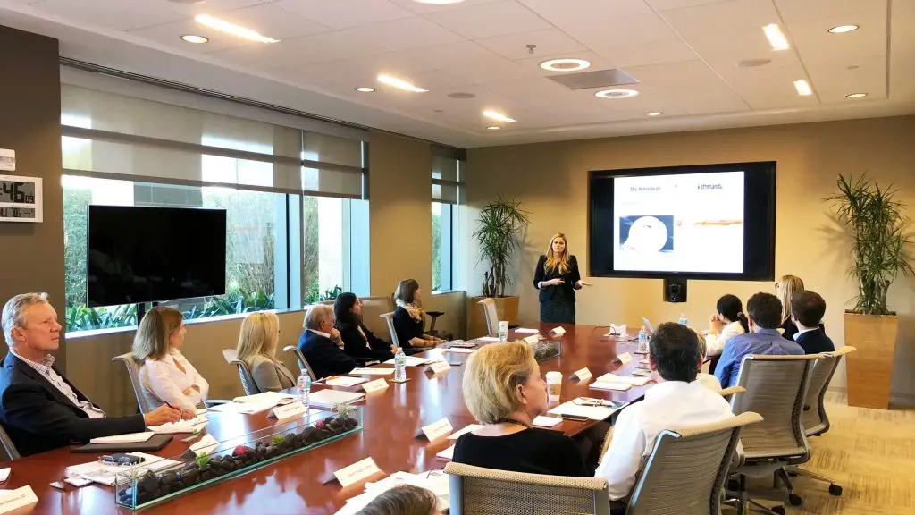 Photo of LJI Board members meeting at the Institute. They are seated around a conference table and viewing a presentation on a large screen