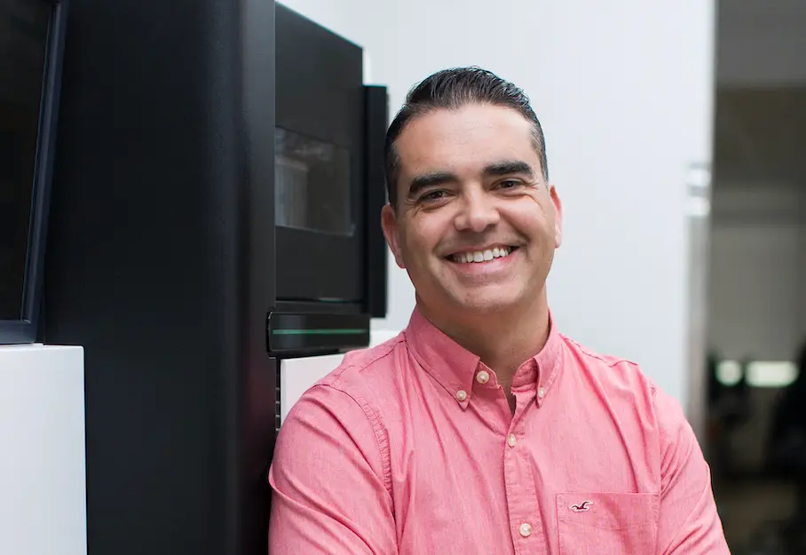 Photo portrait of Gregory Seumois, Ph.D. He is standing in a lab setting and smiling at the camera