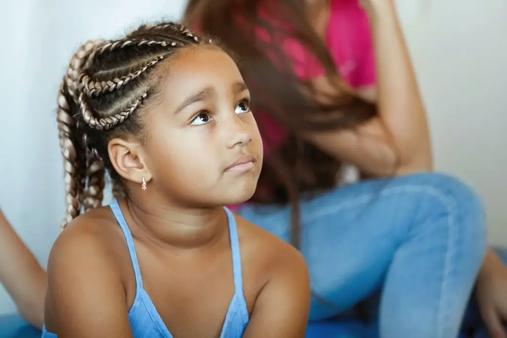 A young girl with braids is carefully watching and listening to some performance.