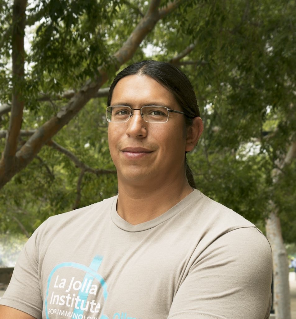 Photo portrait of Enriquez. He is standing outside looking at the camera