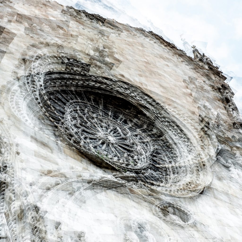 A photo with multiple exposures showing a rose window on the outside of a cathedral. The images overlap to make a swirling pattern.