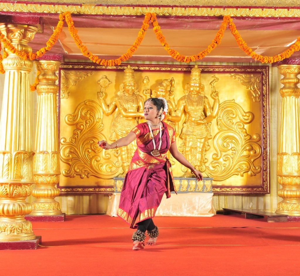 Priyanka Saminathan performs in front of a golden background in her dance regalia