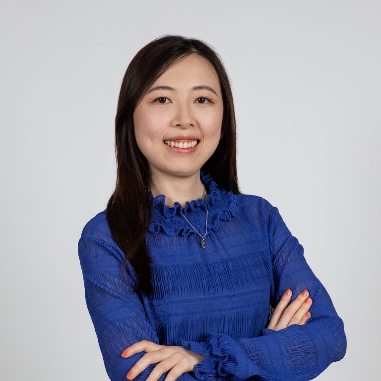 Portrait photo. Fang looks into the camera and smiles. She is wearing a blue top