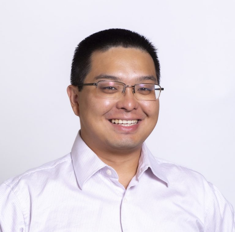 Photo portrait of Zhi. He is against a white backdrop and is smiling at the camera