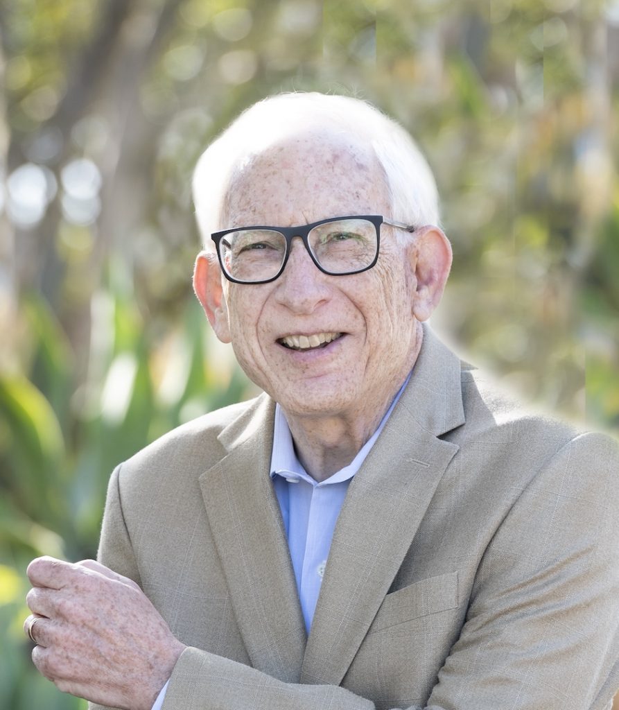 Portrait photo of J. Mark Waxman. He is wearing glasses and a tan suit. He is smiling at the camera