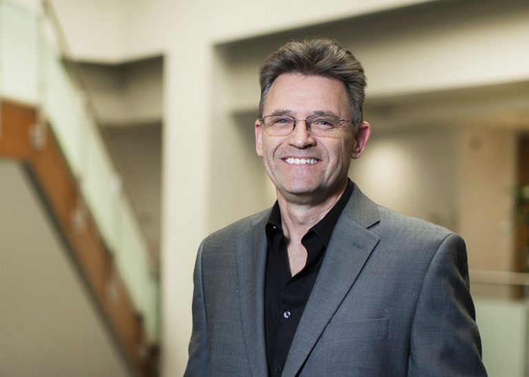 Photo portrait of Dr. Mick Croft. Croft is standing in the LJI Atrium and smiling at the camera