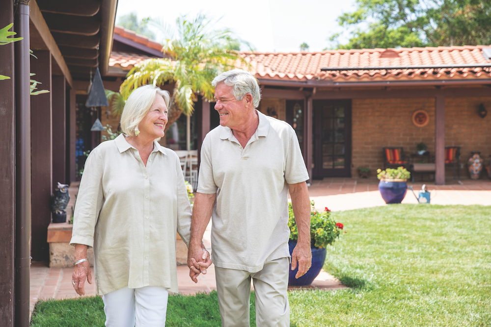 Photo portrait of Raydene and Peter St. Clair. They are holding hands and walking outside their home