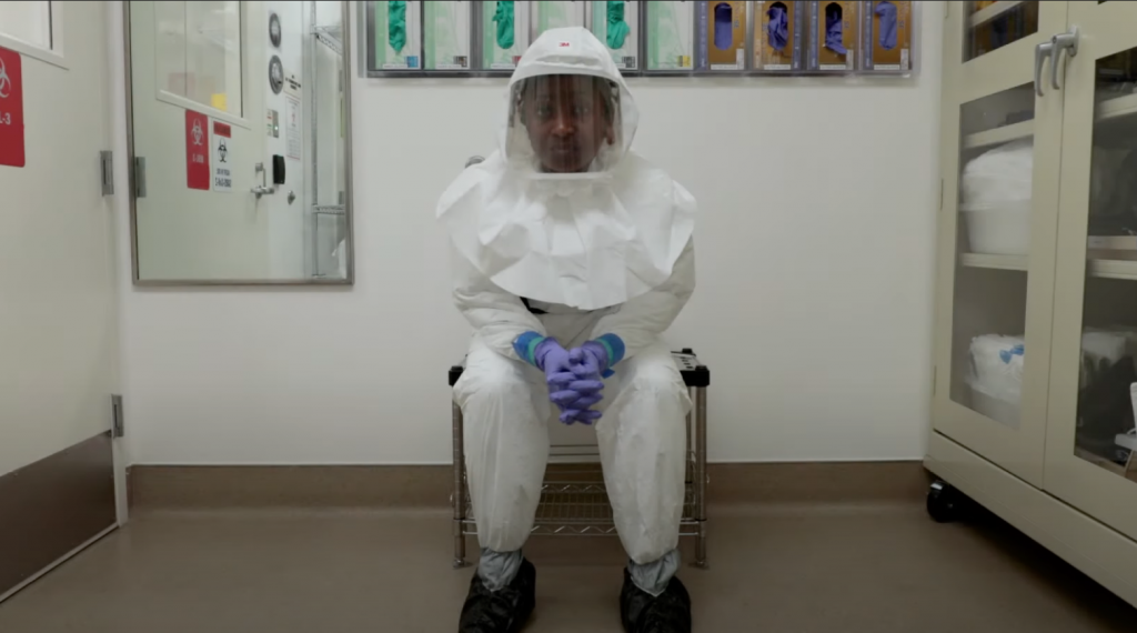 Photo of Annie Elong Ngono in BSL-3 PPE. She is sitting and staring into the camera