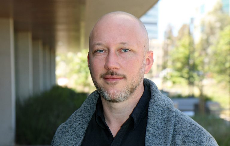 Portrait photo of Sam Myers. He is standing outside and looking at camera