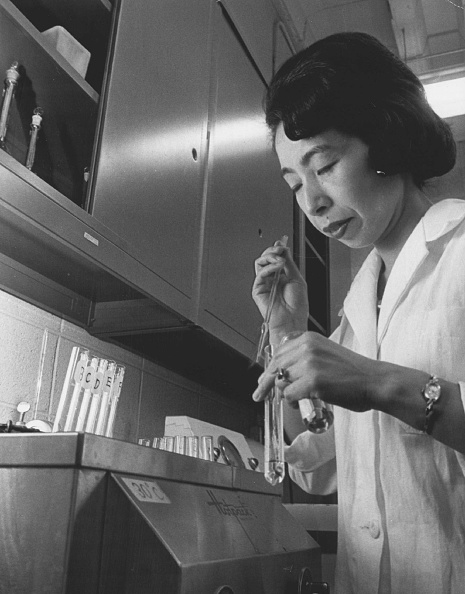 Black and white photo of Ishizaka in a laboratory setting. She is wearing a white lab coat and holding a test tube