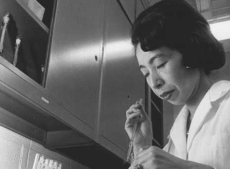 Black and white photo of Ishizaka in a laboratory setting. She is wearing a white lab coat and holding a test tube