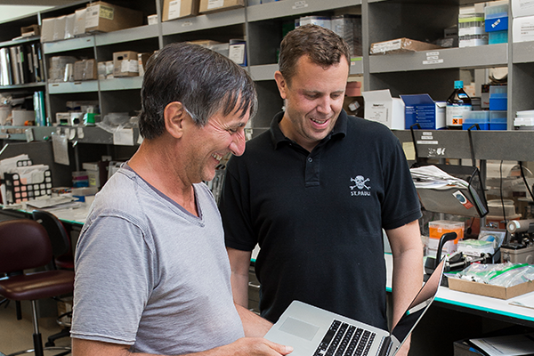 Drs. Sette (left) and Peters stand in a laboratory setting. They are looking at a laptop screen