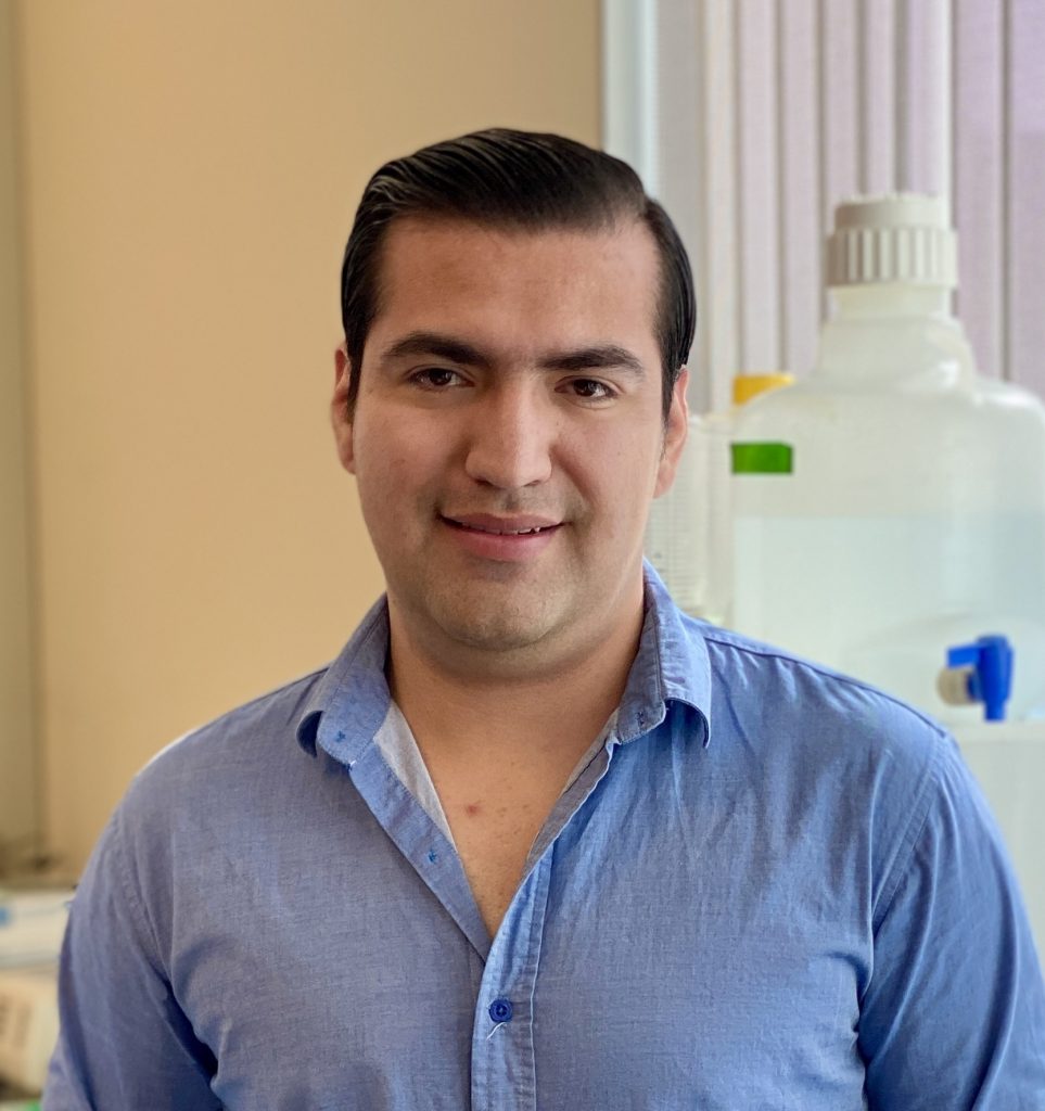 Researcher Job Rocha stands in a laboratory space. Rocha is wearing a blue shirt and is looking at the camera